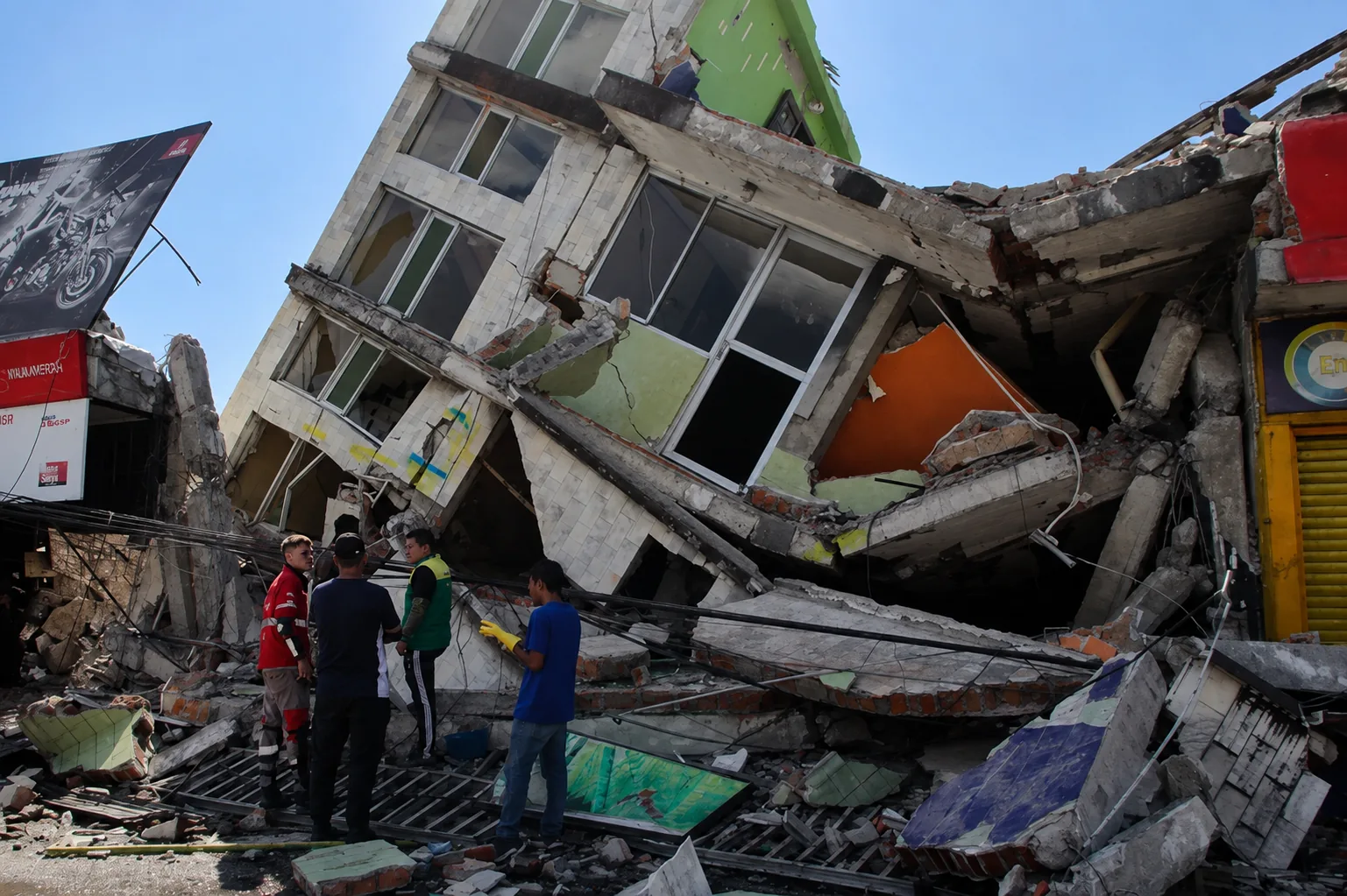 A collapsed building, with rescue crews working at the base